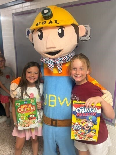 Watkins mascot with two students holding cereal boxes