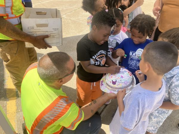 A man in a reflective vest holding a cake for children