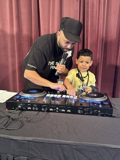 A DJ spinning turntables with a young student