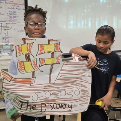 Student holding a cutout of a ship reading "The Discovery"