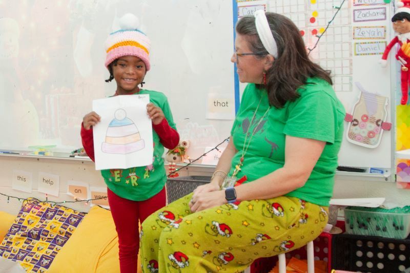 A smiling student holds up her hat design next to the matching handmade beanie she is wearing.