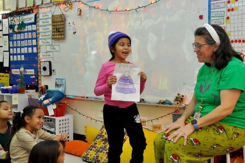 A student proudly presents her purple hat drawing while wearing the matching crocheted beanie.