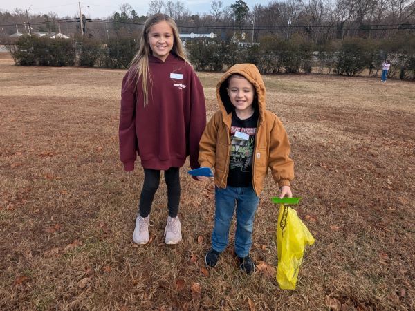 Two students smiling, holding cleaning supplies