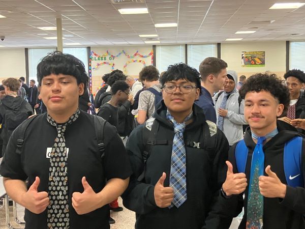Three students wearing ties and giving a thumbs up