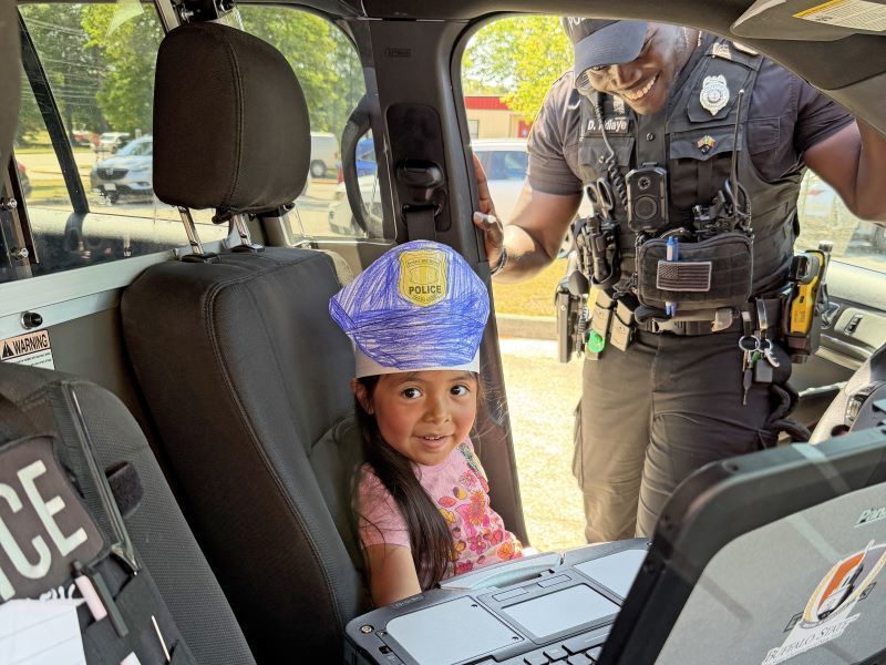 A young student smiling, sitting in the driver's side of a police cruiser
