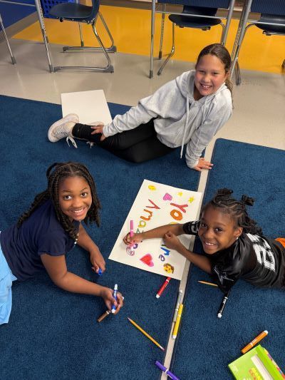 Three girls sitting on the floor, coloring an inspirational poster