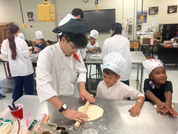 Older student showing a younger student how to roll dough