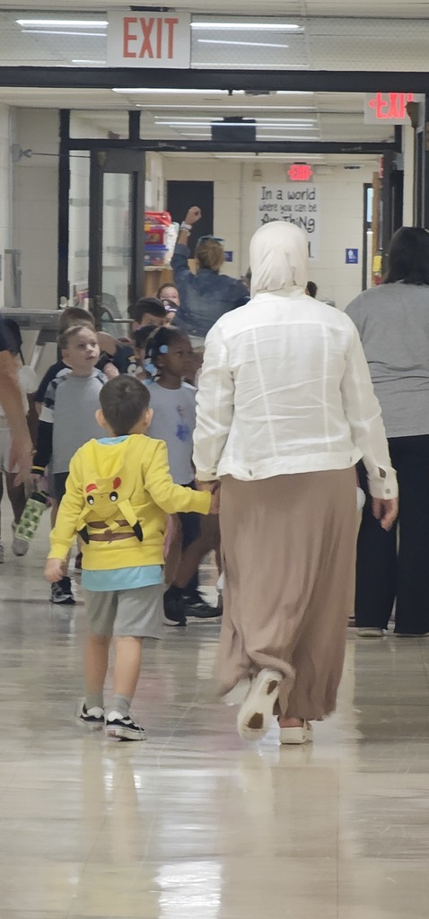Ridge Central Teacher walking with a young student down the school hallway, holding hands.