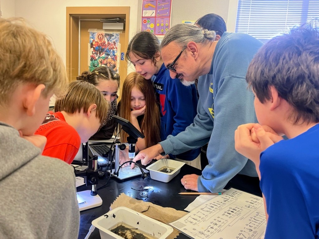 Teacher at Chimacum Junior High School looking at insects under a microscope with his six students.