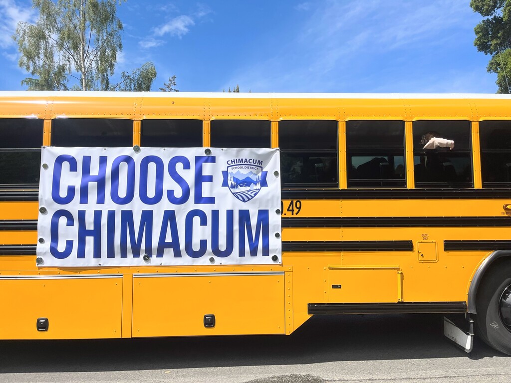 Yellow school bus with a banner on it that says "Choose Chimacum".