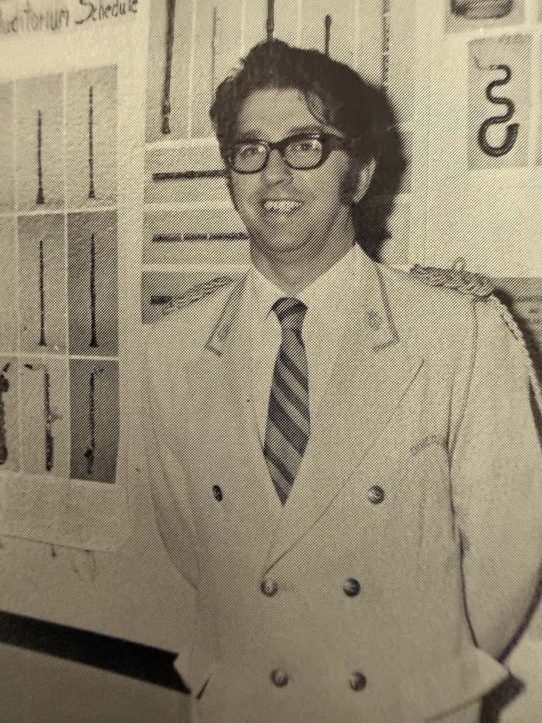 Black and white photo of Duane Montgomery, the beloved Chimacum Band Teacher, wearing a suit and tie, smiling.