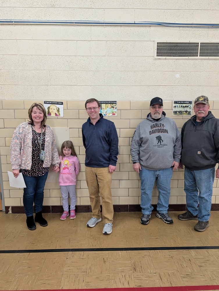 Four adults and one child are standing against a wall.