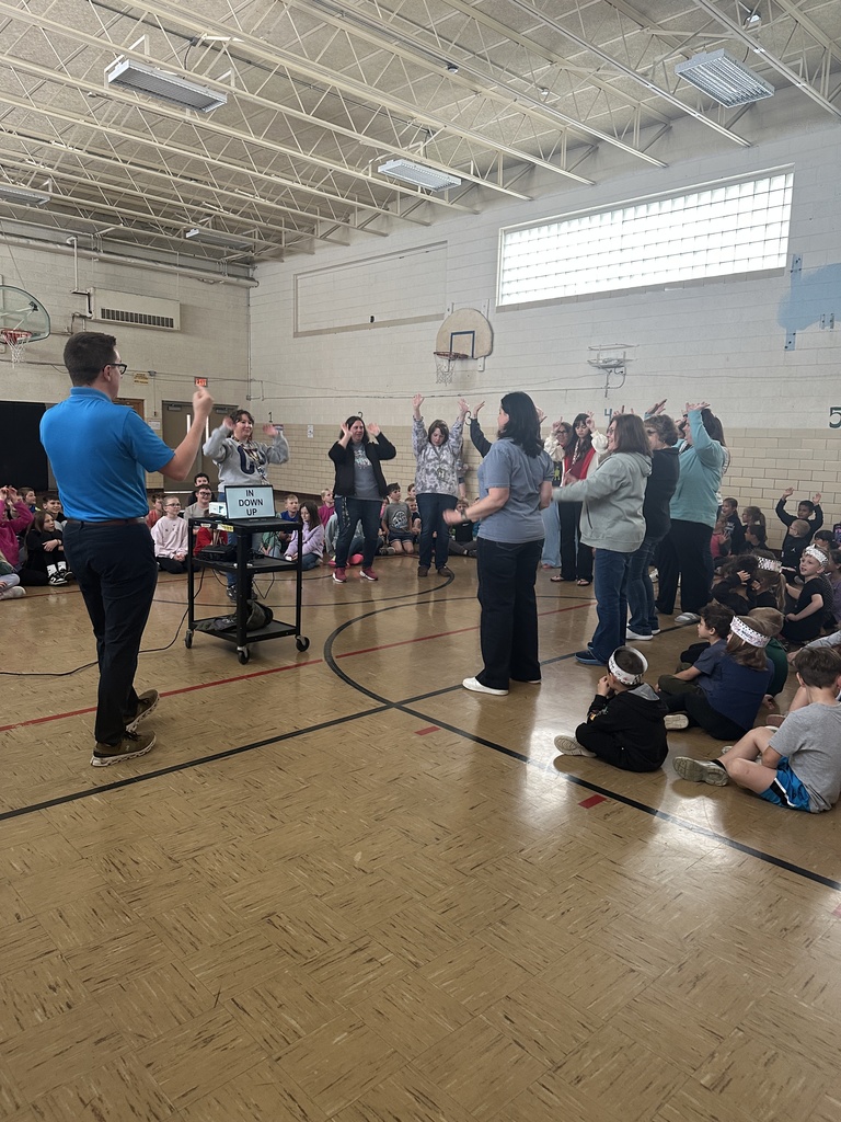Students sitting and staff standing learning the severe weather dance from a meteorologist
