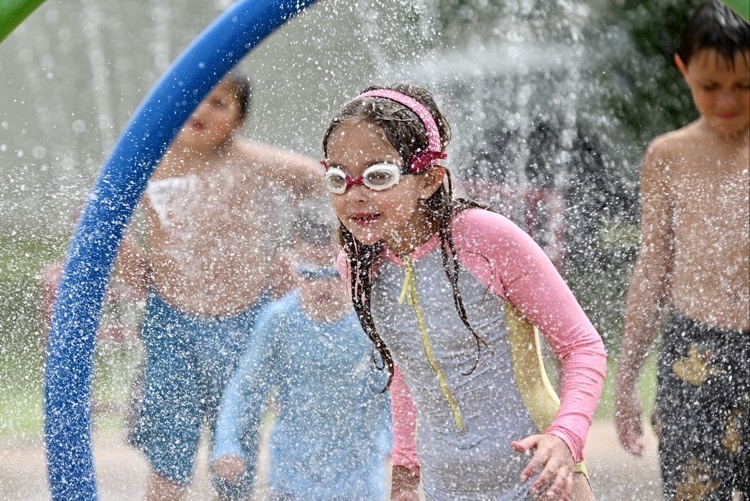 Children play in the water spray features at the Altus Splash Pad while wearing colorful swimsuits and goggles during summer operations at the community splash pad.