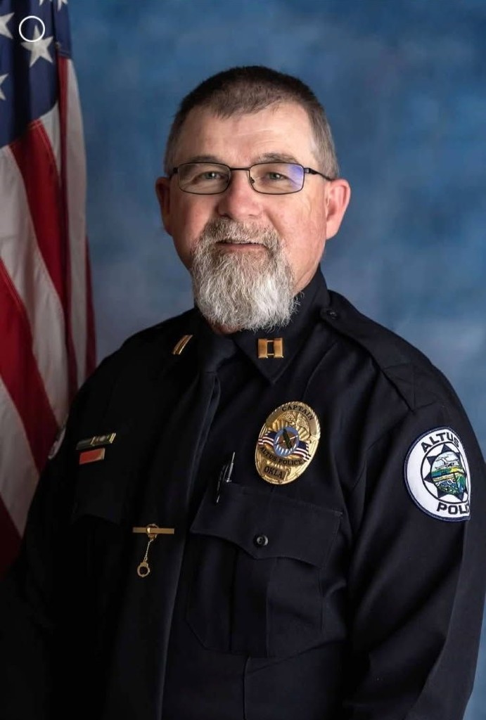 Portrait of Altus Police Captain Chris Barngrover in uniform, standing in front of an American flag.