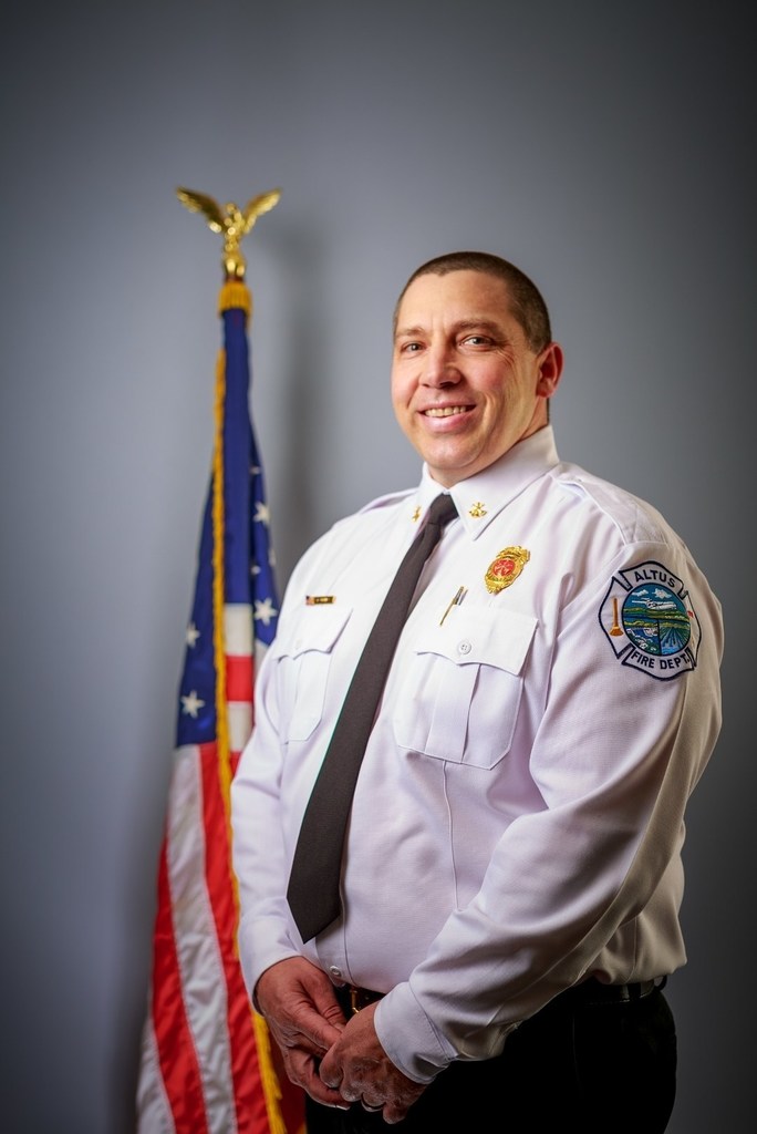 Assistant Fire Chief Benny Barnes in uniform, standing next to the American flag, smiling at the camera.