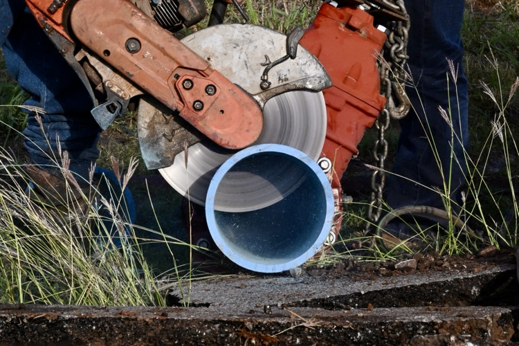 Close-up of a worker cutting into a blue water pipe with a large circular saw during water line maintenance.