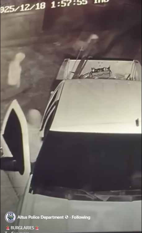 Grainy night-vision surveillance still showing a light-colored vehicle parked with the driver-side door open. A person stands near the open door. A timestamp appears at the top of the frame, and “Altus Police Department” branding is visible at the bottom.