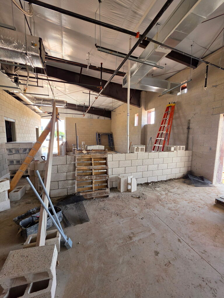 A series of 5 photos showing the interior construction progress of Fire Station No. 3 in Altus. The images feature newly built concrete block walls forming future offices, bedrooms, and work areas. Exposed HVAC ductwork, fire sprinkler piping, electrical systems, and plumbing are visible overhead. Construction materials, scaffolding, ladders, and cinder blocks are positioned throughout the building. One photo shows a construction worker laying concrete blocks while working from scaffolding. Another shows a nearly completed room with finished block walls and a concrete floor. The final image provides a wide view of the station's interior, where room layouts are clearly visible as crews prepare for the next phase of construction, including exterior brick installation. Substantial completion of the project is expected in September 2026.