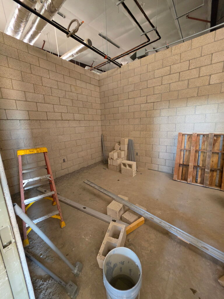 A series of 5 photos showing the interior construction progress of Fire Station No. 3 in Altus. The images feature newly built concrete block walls forming future offices, bedrooms, and work areas. Exposed HVAC ductwork, fire sprinkler piping, electrical systems, and plumbing are visible overhead. Construction materials, scaffolding, ladders, and cinder blocks are positioned throughout the building. One photo shows a construction worker laying concrete blocks while working from scaffolding. Another shows a nearly completed room with finished block walls and a concrete floor. The final image provides a wide view of the station's interior, where room layouts are clearly visible as crews prepare for the next phase of construction, including exterior brick installation. Substantial completion of the project is expected in September 2026.