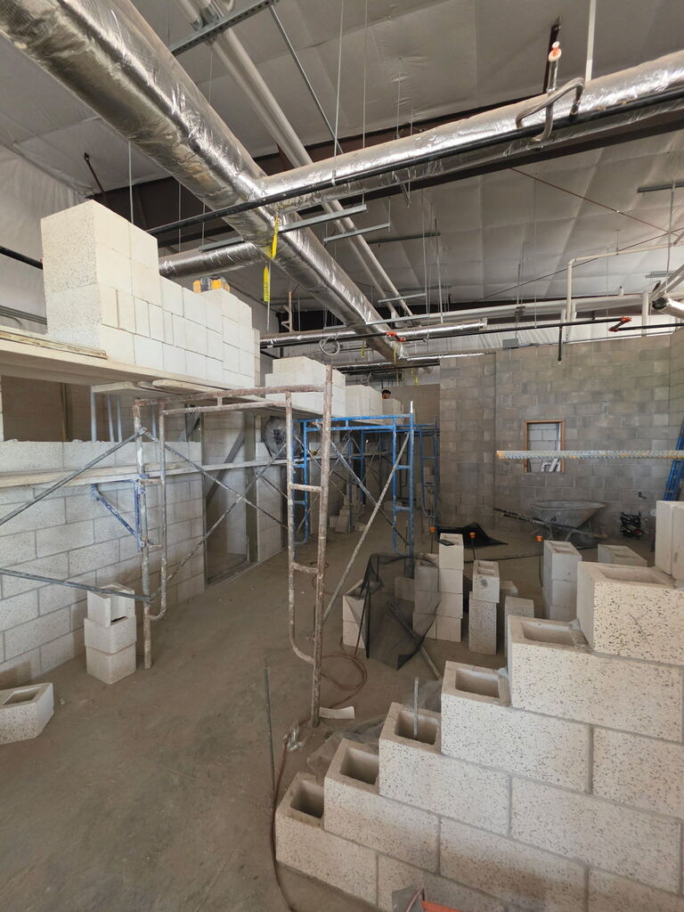 A series of 5 photos showing the interior construction progress of Fire Station No. 3 in Altus. The images feature newly built concrete block walls forming future offices, bedrooms, and work areas. Exposed HVAC ductwork, fire sprinkler piping, electrical systems, and plumbing are visible overhead. Construction materials, scaffolding, ladders, and cinder blocks are positioned throughout the building. One photo shows a construction worker laying concrete blocks while working from scaffolding. Another shows a nearly completed room with finished block walls and a concrete floor. The final image provides a wide view of the station's interior, where room layouts are clearly visible as crews prepare for the next phase of construction, including exterior brick installation. Substantial completion of the project is expected in September 2026.