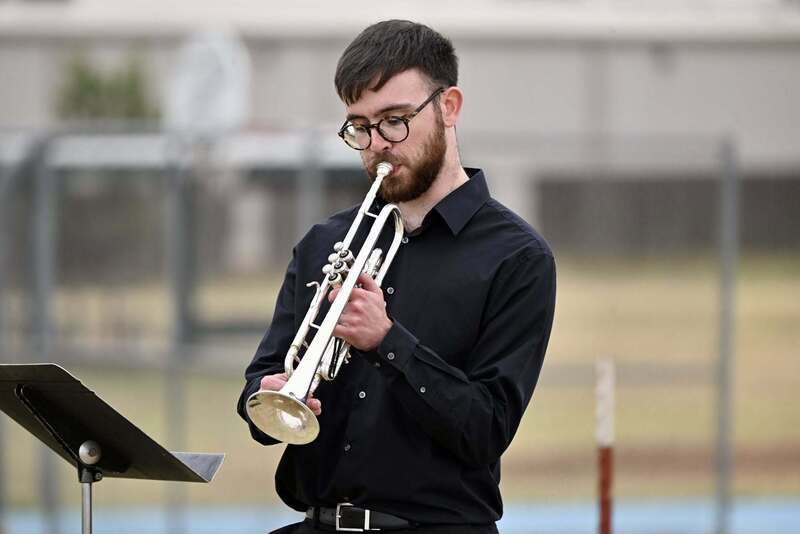 A musician in a black shirt plays trumpet outdoors during the Ceremonial Raising of the Colors.