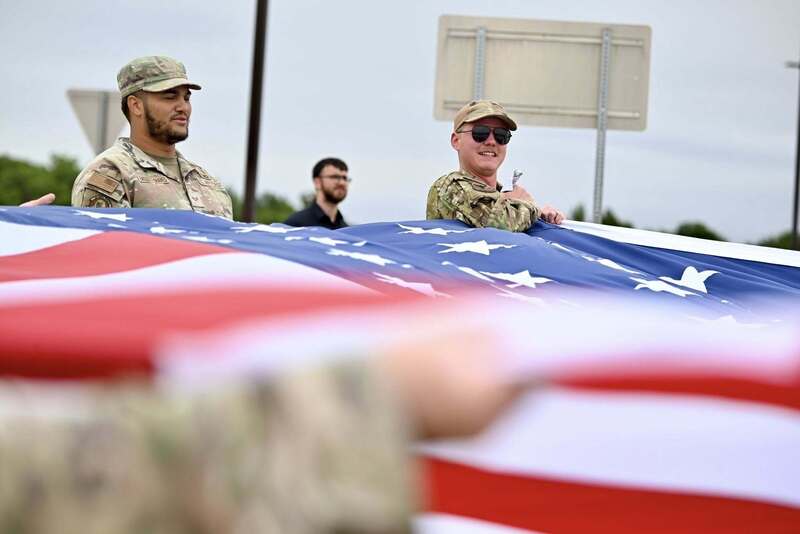 Service members stand behind a large American flag during preparations for the Ceremonial Raising of the Colors.