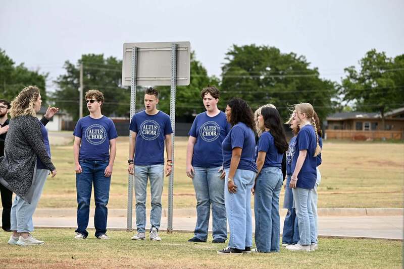 Altus Choir members wearing blue shirts sing outdoors during the Ceremonial Raising of the Colors.