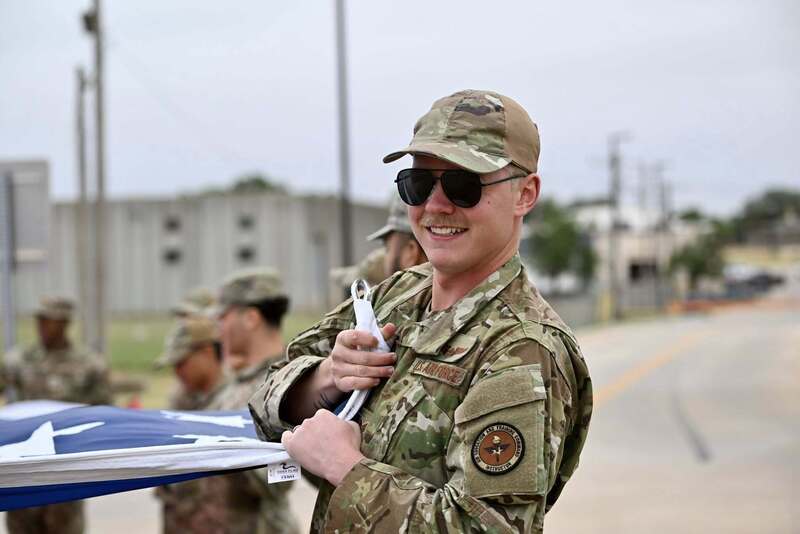 A uniformed service member smiles while holding part of a large American flag before the raising ceremony.
