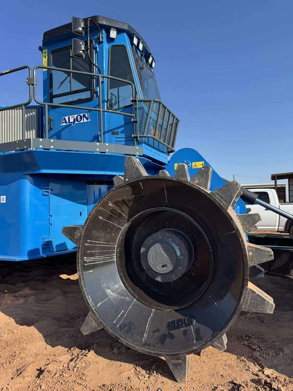 Close-up of the spiked front wheel on the Aljon 500 landfill compactor, with the operator cab and railing visible in the background.