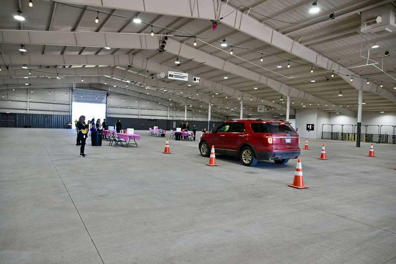 A red SUV drives through a vaccination station set up inside the Jackson County Expo Center, with staff members and orange cones guiding vehicles during the flu vaccine drive-thru event.