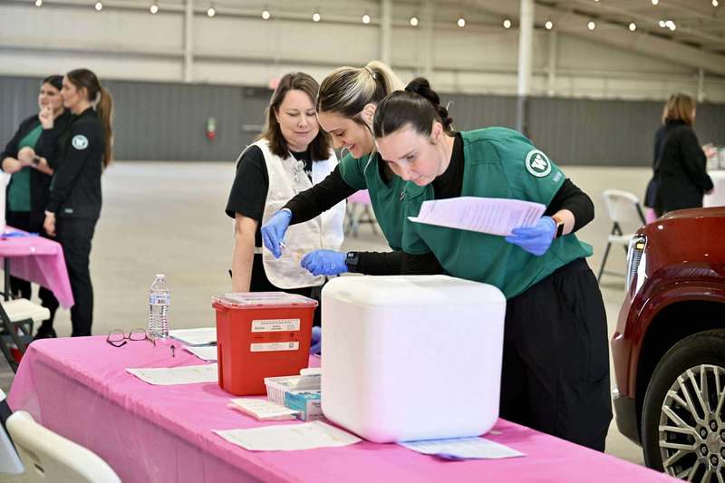 Three healthcare workers prepare vaccine supplies at a pink-covered table inside the Jackson County Expo Center during the flu vaccine drive-thru event.