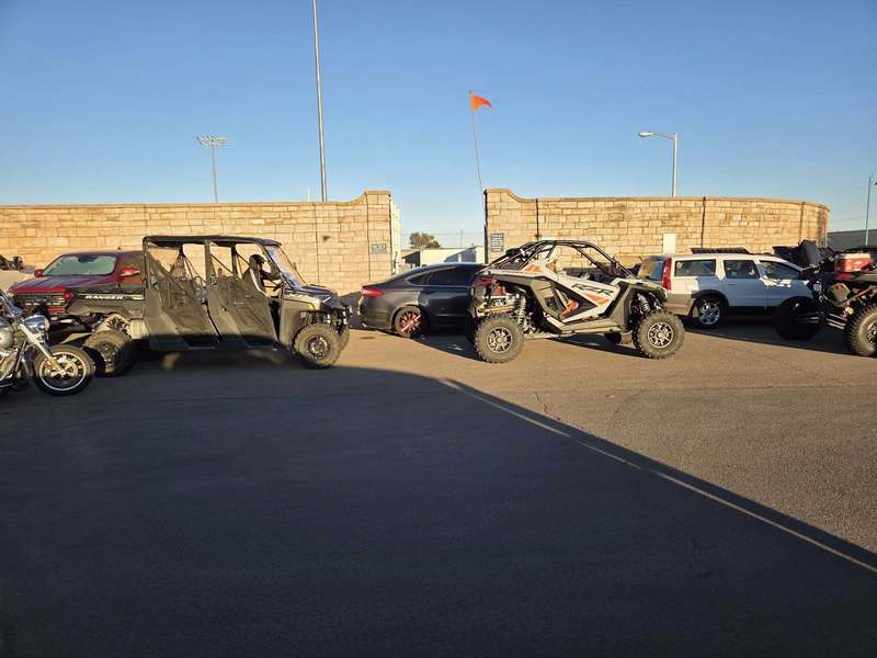 Off-road vehicles lined up in a parking lot during sunset as part of a community birthday parade gathering in Altus.