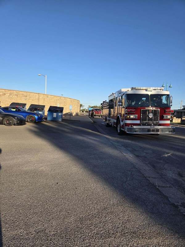 An Altus fire truck parked along a sunny street with community members gathering nearby for a birthday parade.