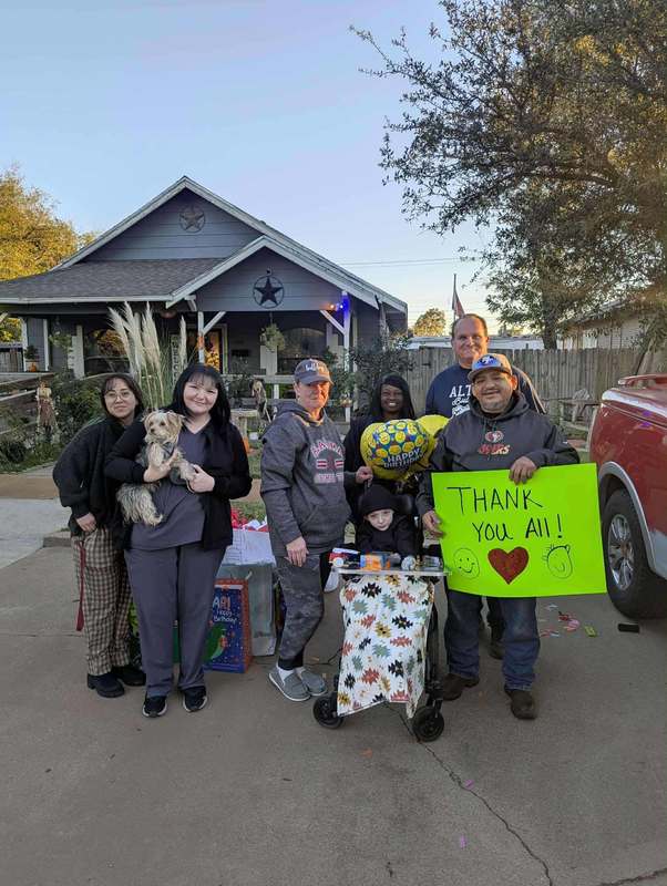 Family and Neighbors stand outdoors holding bright signs and gifts while visiting to celebrate a young boy’s 10th birthday.
