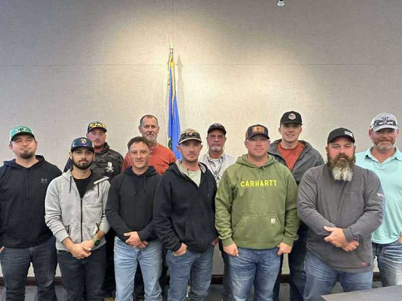 Group photo of Altus Electric Department team members standing together indoors during the MESO Apprentice Lineman School event, with the Oklahoma state flag visible behind them.