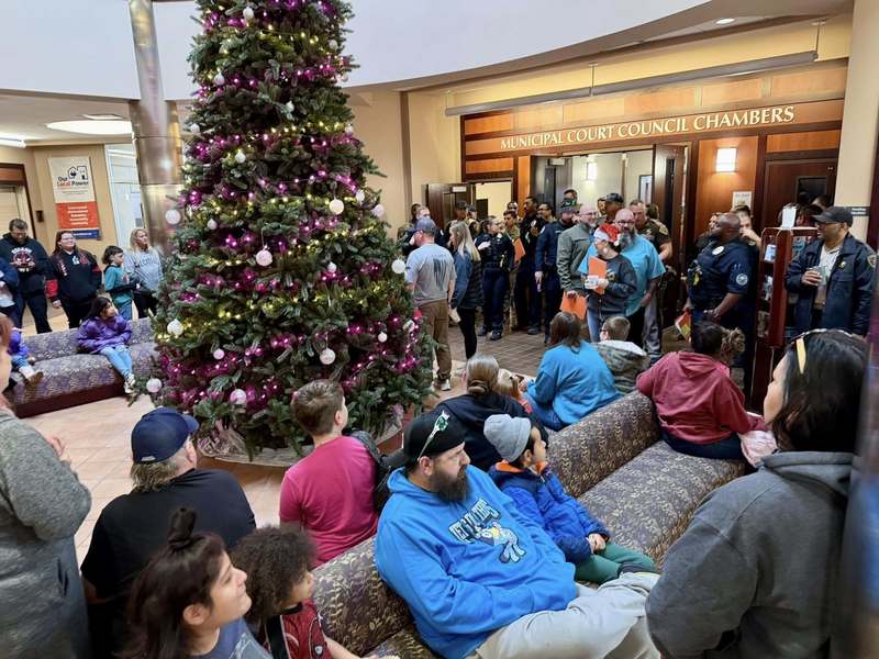 Children sit together during the Cops and Kids Christmas event while officers and volunteers stand nearby.