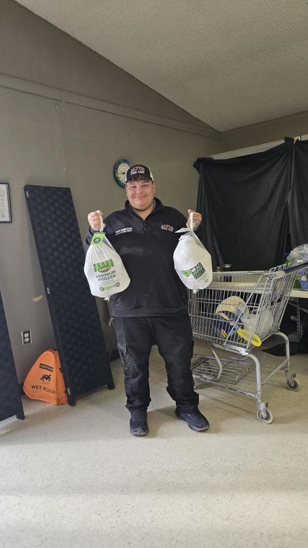 Firefighter stands indoors holding a gift card near tables of coat drive supplies.