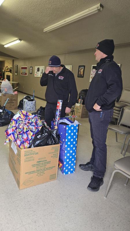 Firefighter stands near donation items and a pile of coats during the coat drive.