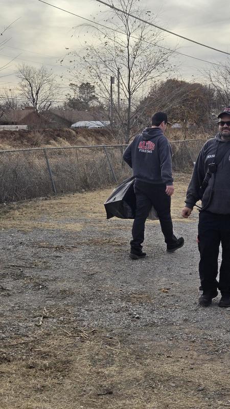 Firefighter walks across a gravel area carrying a bag of donated coats.