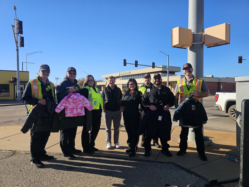 Altus Fire and EMS staff and volunteers stand at a street corner holding winter coats for Coats for Kids.