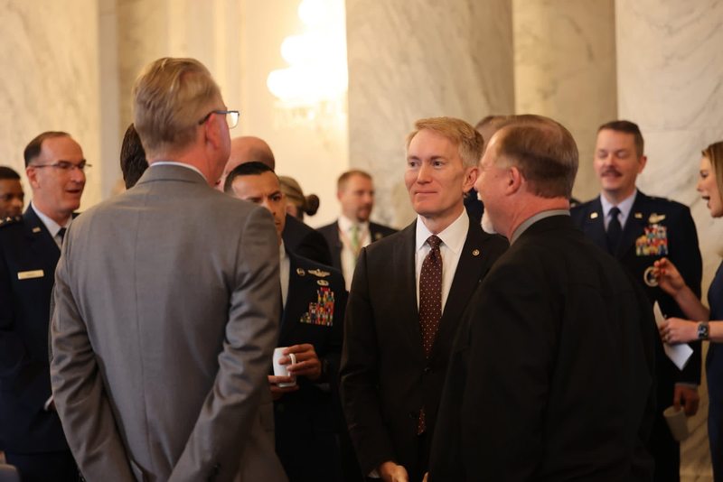 A group of men, including military personnel and officials in suits, engage in conversation during a formal gathering.
