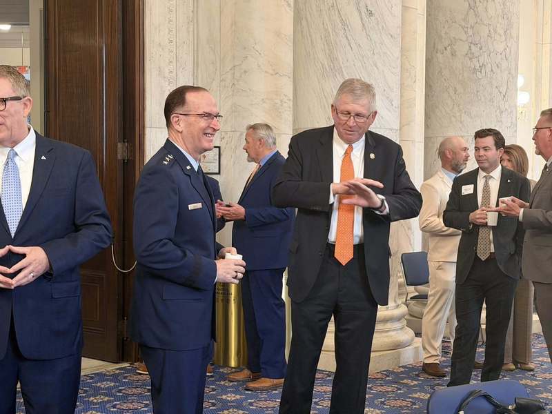 Several men in suits and military uniforms stand in a small group, talking and holding drinks during a networking event.
