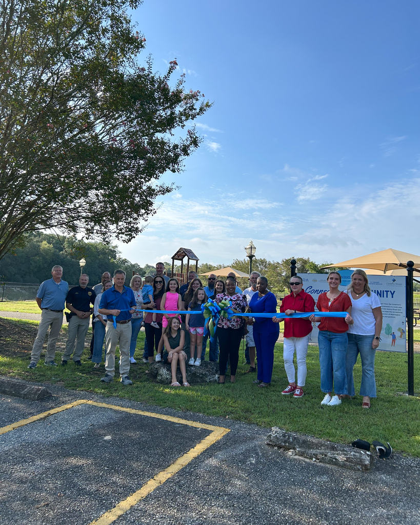 group photo of City  staff, elected officials, and community members in front of Andrews Street Park holding blue and green ribbon