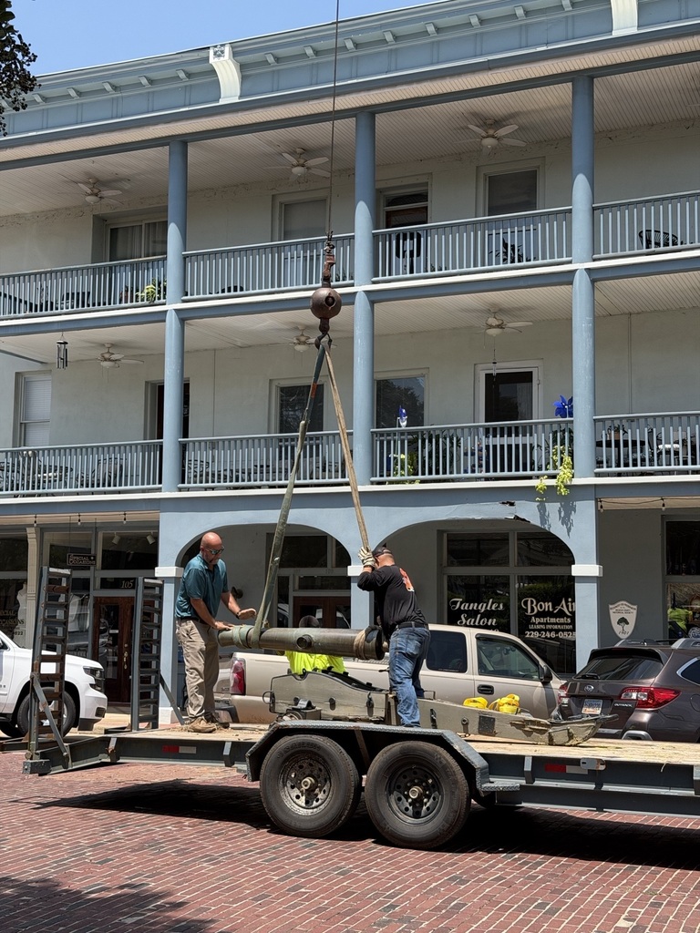 two men on a flat bed trailer and one man on the ground work to load a civil war era cannon onto the trailer