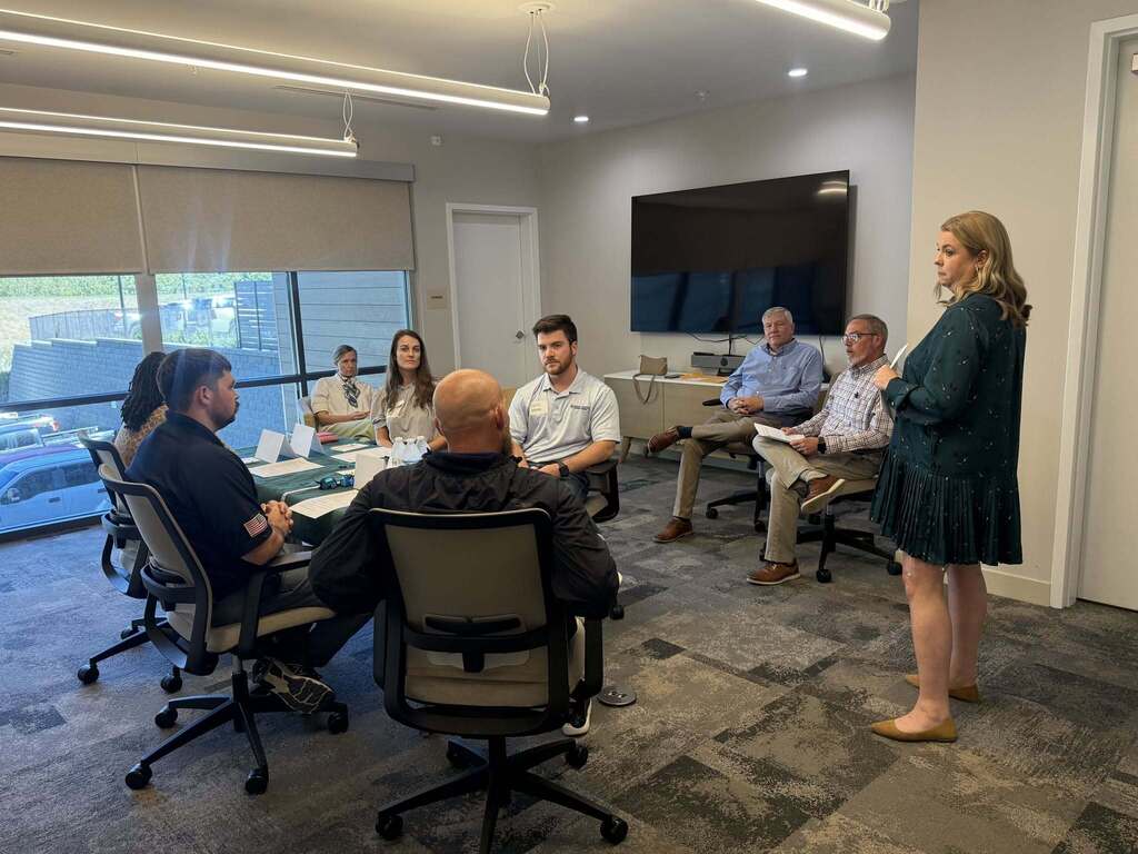 Leadership Decatur County participants take part in a mock open meeting activity to gain a better understanding of local government procedures. A woman stands and addresses the group while other participants sit around a conference table.