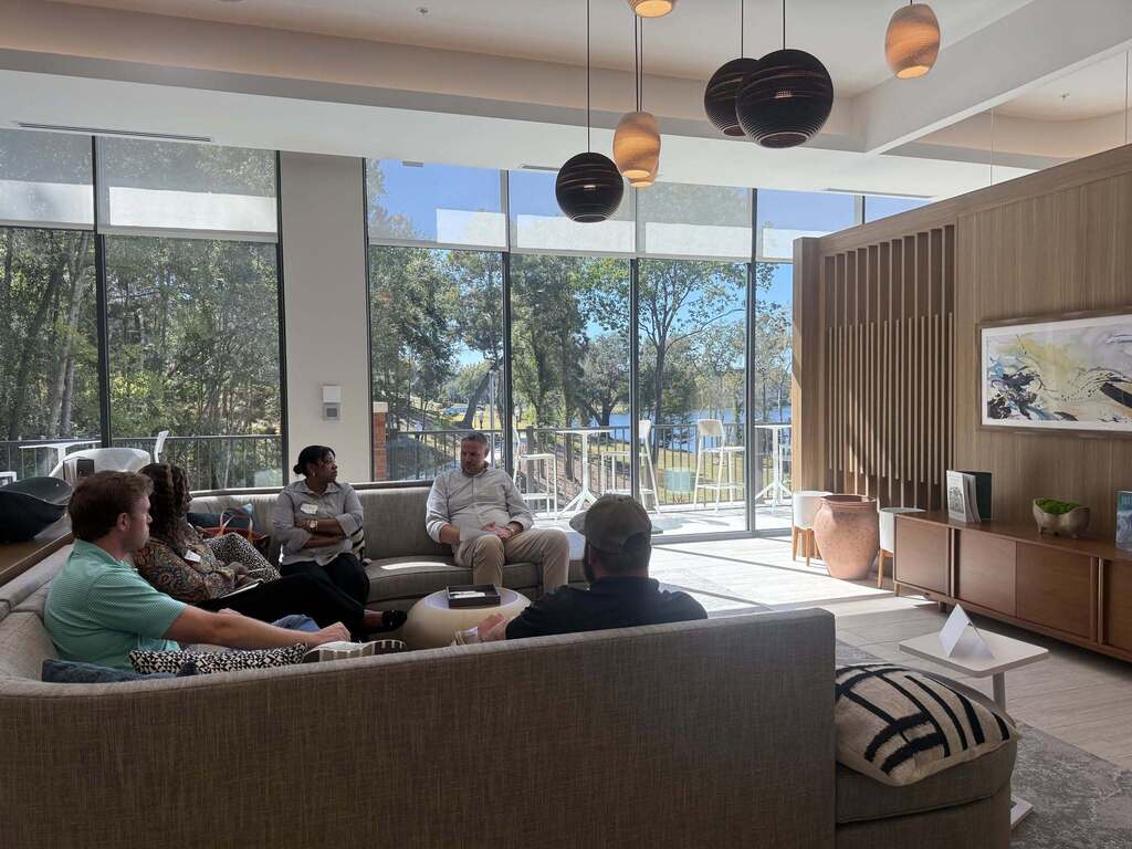 Leadership Decatur County participants engage in a small group discussion with a local government representative in a bright meeting area overlooking the water. Five participants sit together on couches while discussing local government operations.