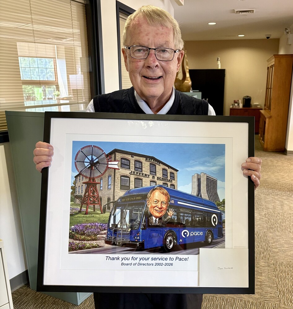 Mayor Jeffery D. Schielke holds an illustration of himself in a bus with City hall in the background