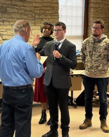 Alderperson Alan Wolff delivers the oath of office to Logan Perry. Two supporters stand behind Perry.