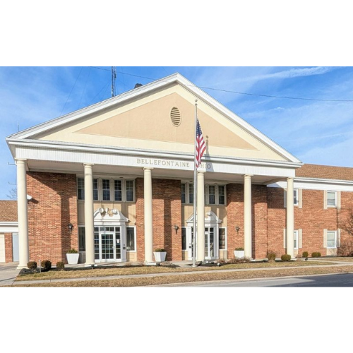 A brick building with white columns and an American flag at the entrance, marked "Bellefontaine." The sky is clear, suggesting a sunny day.